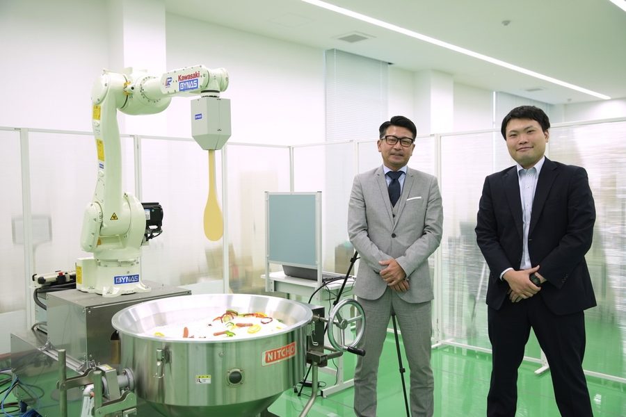 ロボットの横でバイナス社の社員2名が並んでいる様子